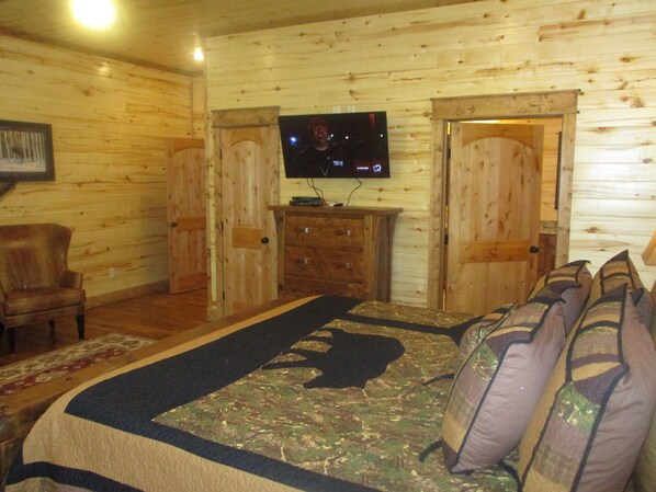 Una habitación tipo cabaña de madera con una cama, un televisor, una silla y un aparador.