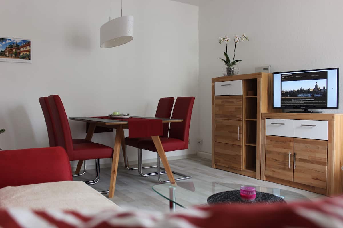 A modern room with a dining table, red chairs, a TV, and a wooden cabinet.