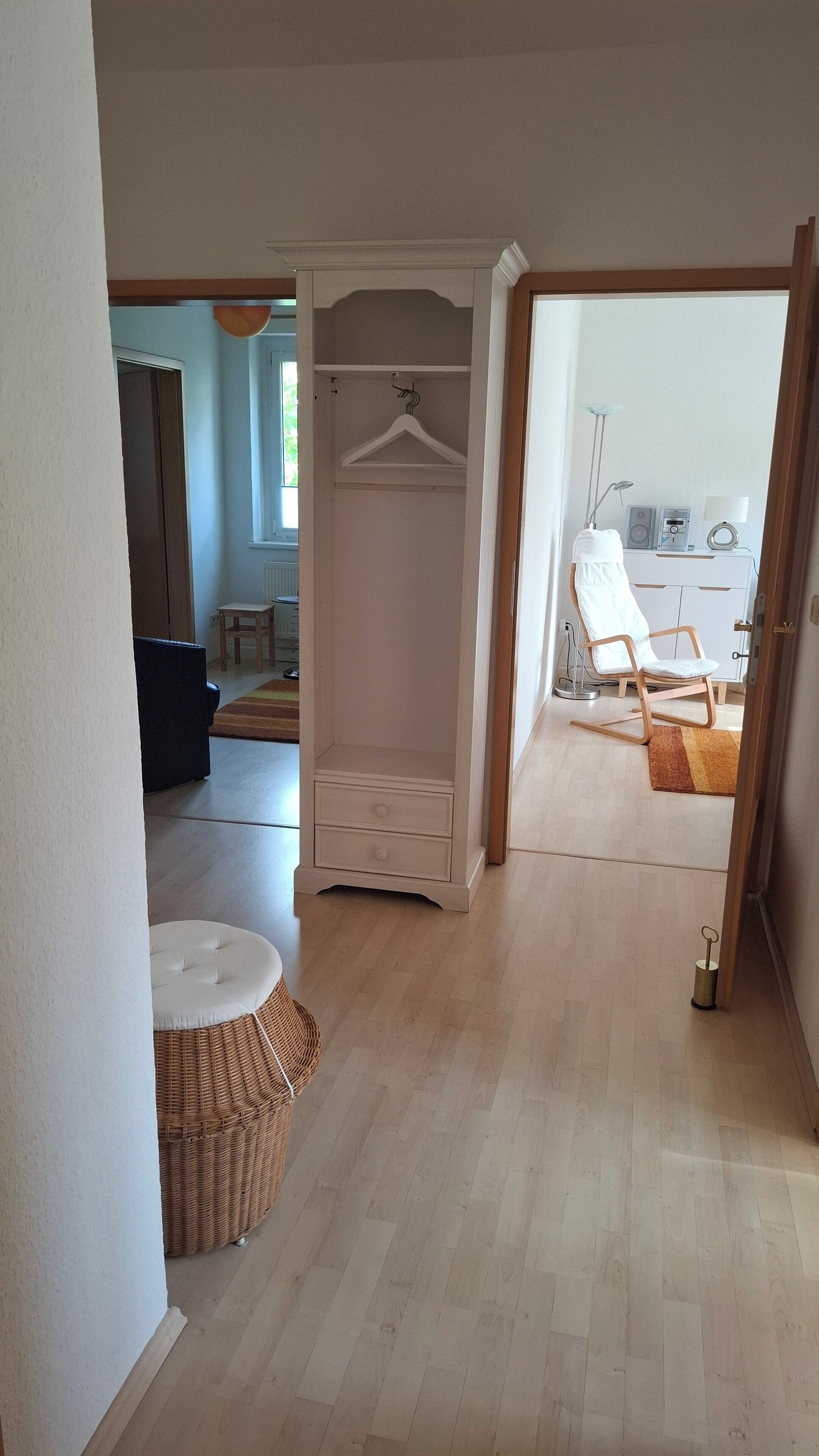 Un pasillo con un armario, una silla de mimbre y vistas a una habitación con una silla y una mesa.