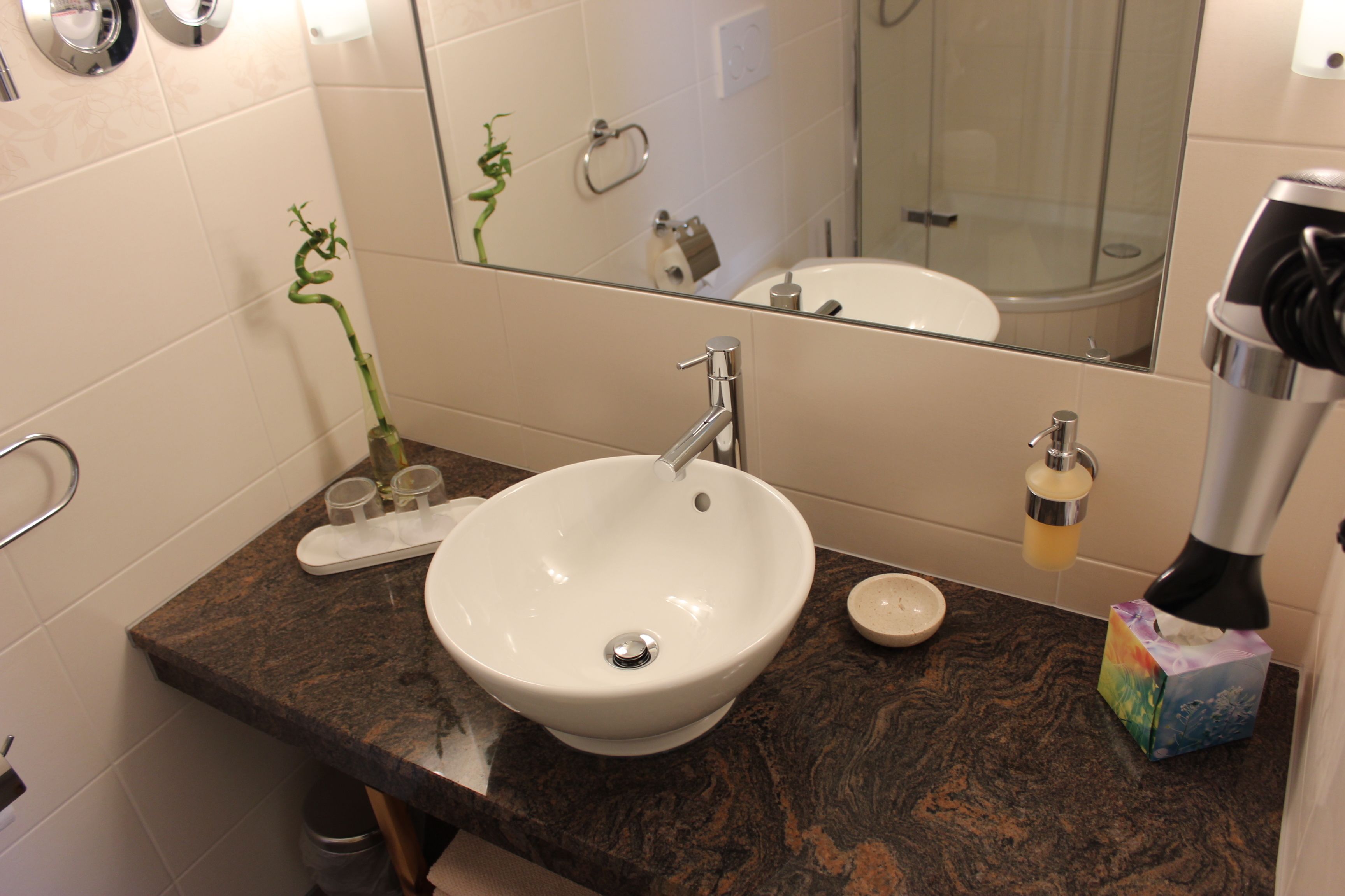 A bathroom with a white sink, dark marble countertop, and a mirror reflecting a shower area.