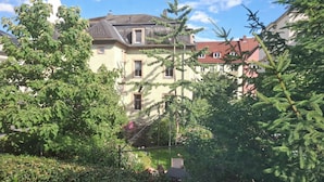 Un edificio residencial con múltiples ventanas, un balcón y un jardín con diversas plantas y flores.