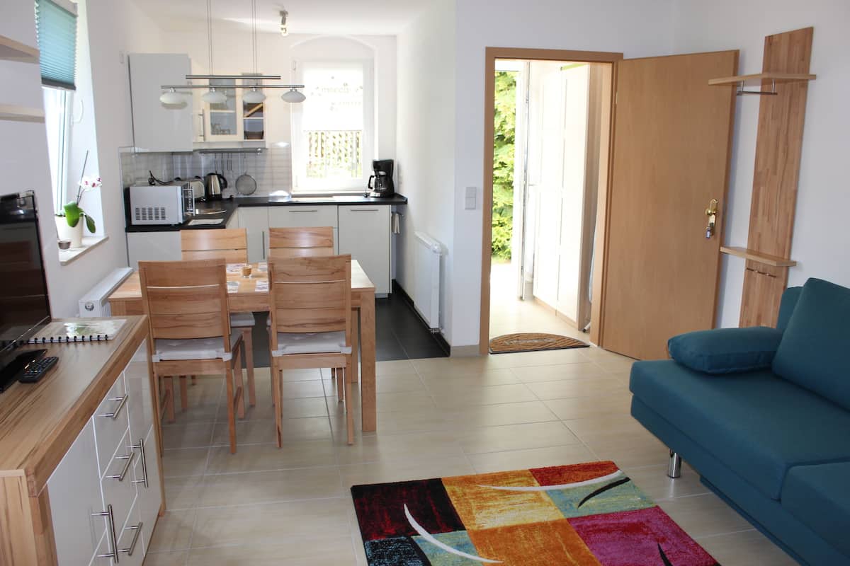 A modern kitchen with white cabinets, a dining table with chairs, a blue sofa, and a colorful rug.