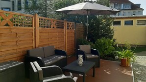 Un patio al aire libre con cerca de madera, dos sofás, una mesa y una sombrilla.