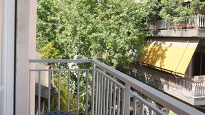 Een balkon met een tafel en stoelen, een leuning en uitzicht op bomen en gebouwen.