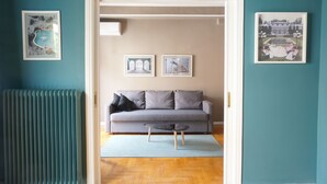 Een woonkamer met een grijze bank, een bijzettafeltje en lijstjes met foto's aan teal muren.