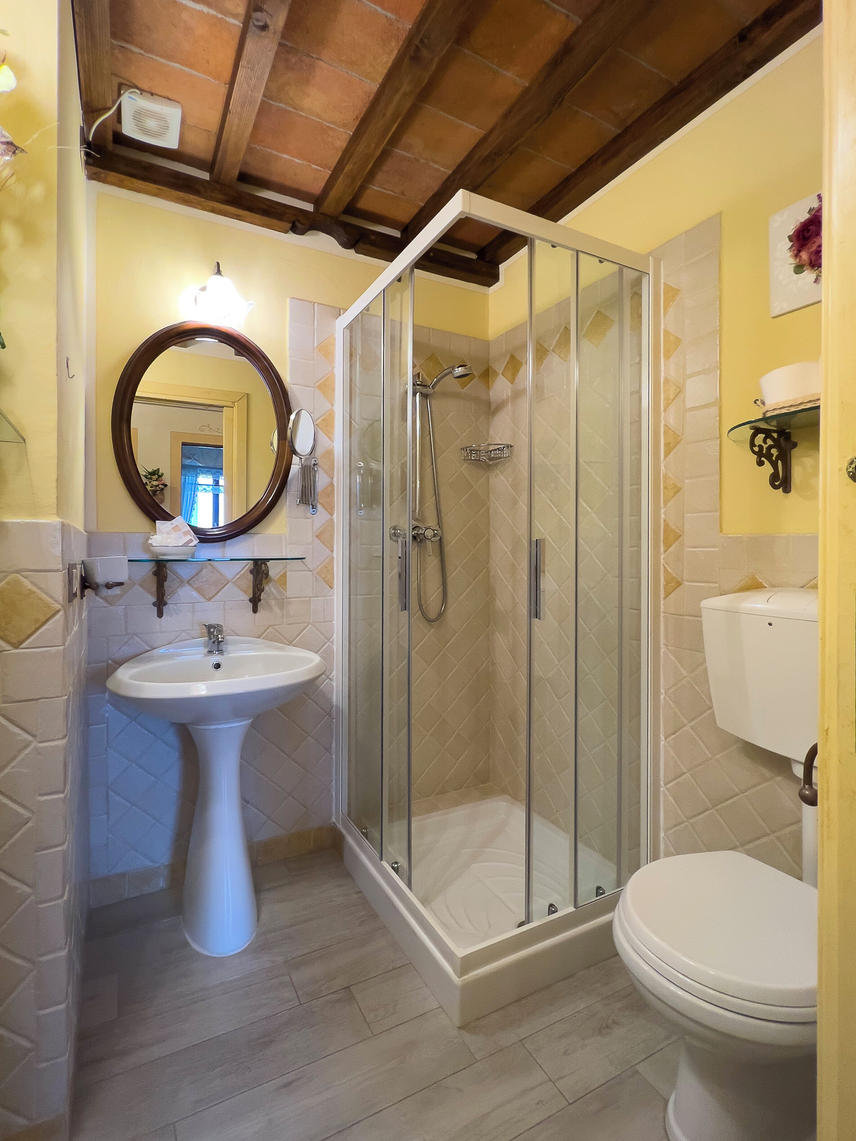 A bathroom with a glass-enclosed shower, a pedestal sink, and a toilet.