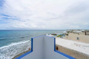 A coastal view from a balcony with a clear sky, overlooking the sea and a residential area with buildings.