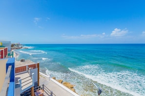 Una vista sulla costa con cielo sereno, un edificio con balcone che si affaccia sul mare e una costa rocciosa.