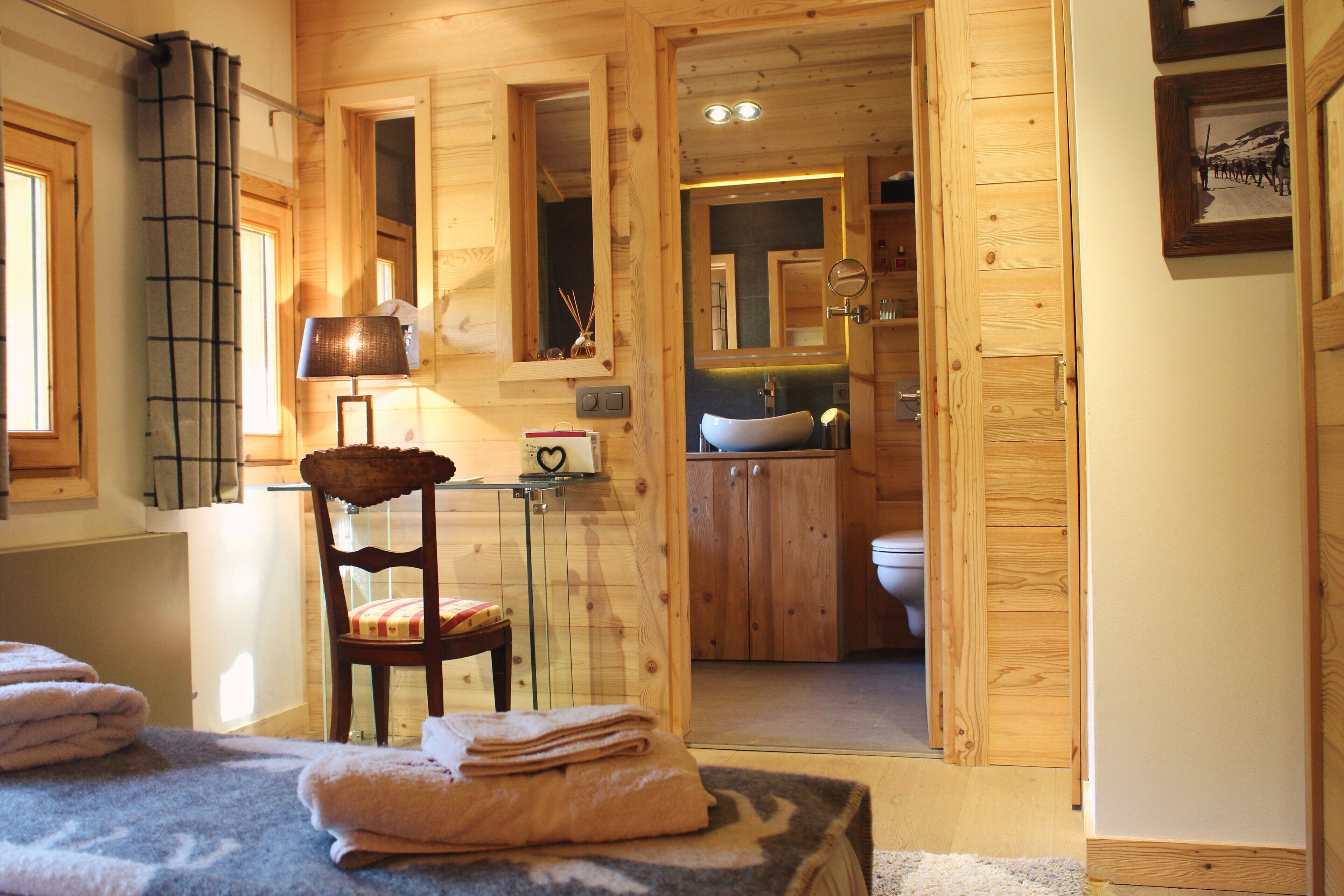 Ein Schlafzimmer einer Holzhütte mit einem Bett, einem Sessel, einer Lampe und einem durch eine offene Tür einsehbaren Badezimmer.