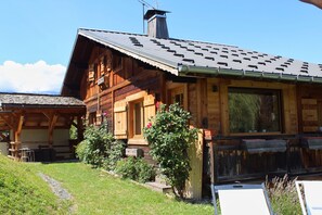 Una baita di legno con tetto spiovente, un camino e un portico con posti a sedere.