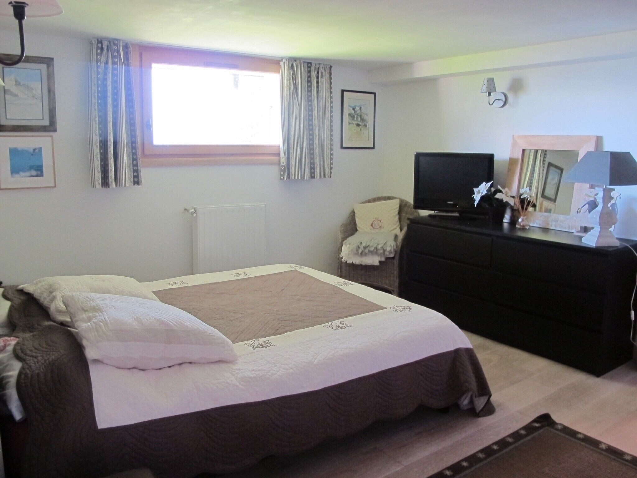 A bedroom with a bed, a dresser, a television, and a window with curtains.