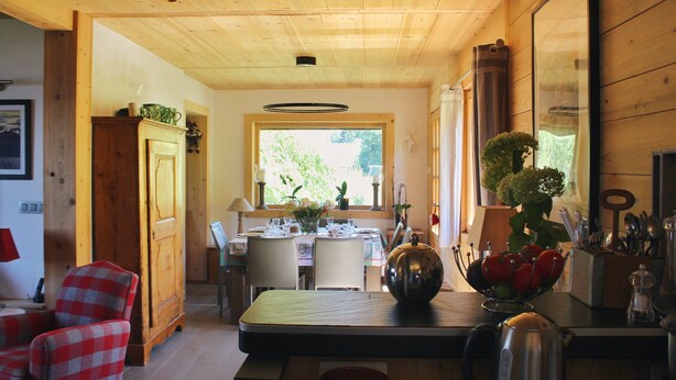 Interior de madera con una mesa de comedor, sillas y una zona de cocina con utensilios.