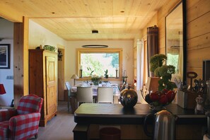 A wooden interior with a dining table, chairs, and a kitchen area with utensils.