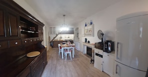 Una cocina con armarios de madera, una mesa de comedor con sillas, un refrigerador blanco y un microondas.