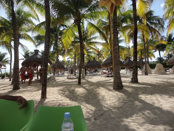 Une plage bordée de palmiers et ombragée par des parasols en feuilles de palmier.