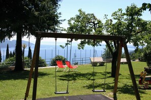 Une balançoire en bois avec deux sièges, un banc et une vue sur un lac et des montagnes en arrière-plan.