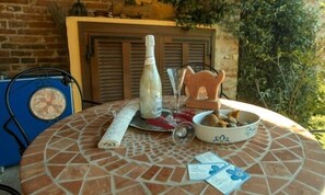 Una mesa redonda con un diseño de mosaico, una botella, un vaso, un cuenco con aperitivos y un pequeño objeto azul sobre la mesa.