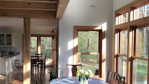 A spacious dining area with a round table, wooden chairs, and a view of the outdoors through large windows.
