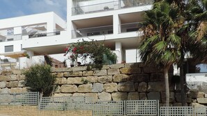 A modern multi-story building with balconies, a stone retaining wall, and a palm tree. -  Marina de Casarès Dona Julia Golf Andalusia 29690 ES (Casarès costa-malaga andalousie)