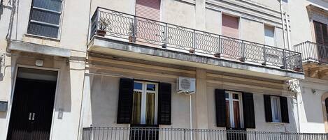 A two-story building with a balcony, a closed door, and an air conditioning unit.