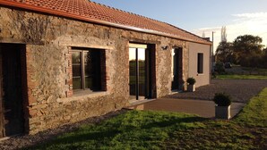 A stone building with a tiled roof, large windows, and a paved driveway. - Le Pressoir: Spacious vacation rental, surrounded by nature, forest 50 meters away, Pornic 20 minutes away (Chaumes-En-Retz)