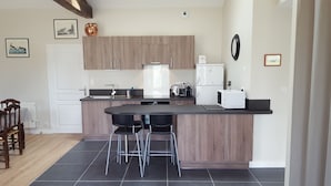 A modern kitchen with a central island, bar stools, and a dining area with a wooden table and chairs. - Le Pressoir: Spacious vacation rental, surrounded by nature, forest 50 meters away, Pornic 20 minutes away (Chaumes-En-Retz)