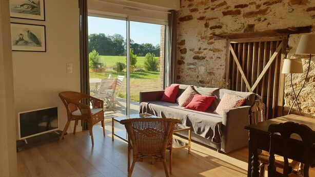 A cozy living room with a sofa, two wicker chairs, a table, and a large window offering a view of a green field. - Le Pressoir: Spacious vacation rental, surrounded by nature, forest 50 meters away, Pornic 20 minutes away (Chaumes-En-Retz)