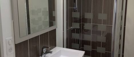 Un baño moderno con lavamanos blanco, espejo y ducha con mampara de vidrio.