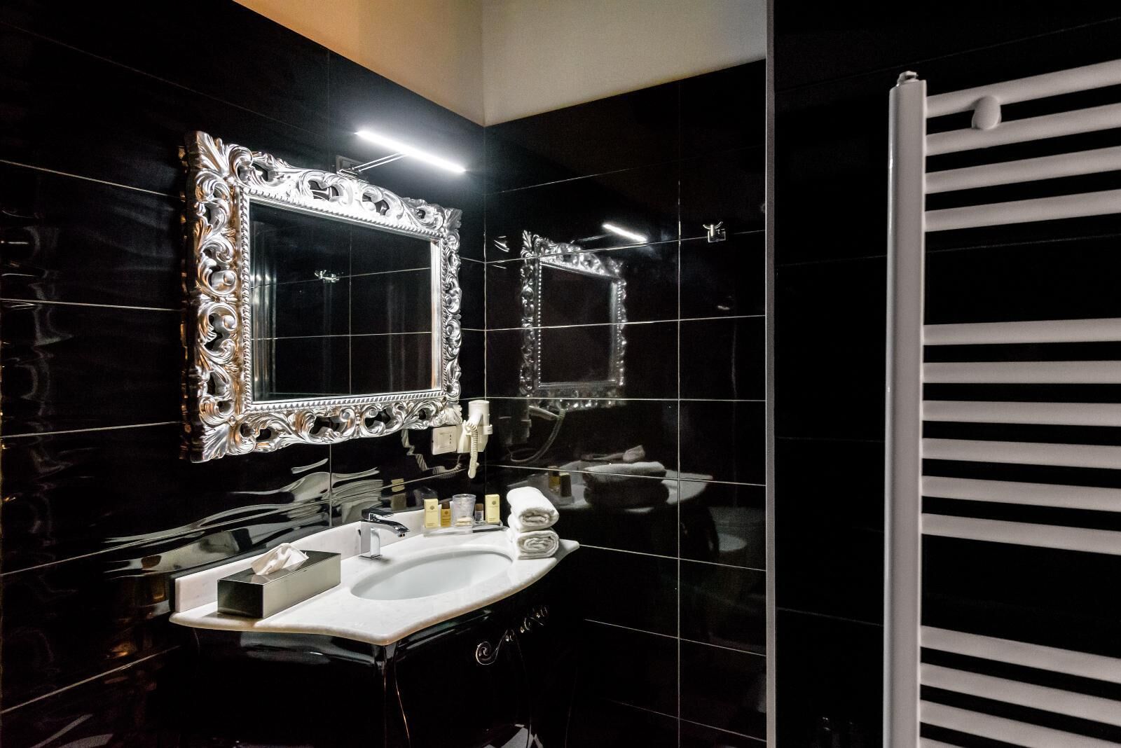 Ein modernes Badezimmer mit einem großen Spiegel, schwarzen Fliesenwänden und einer weißen Badewanne.