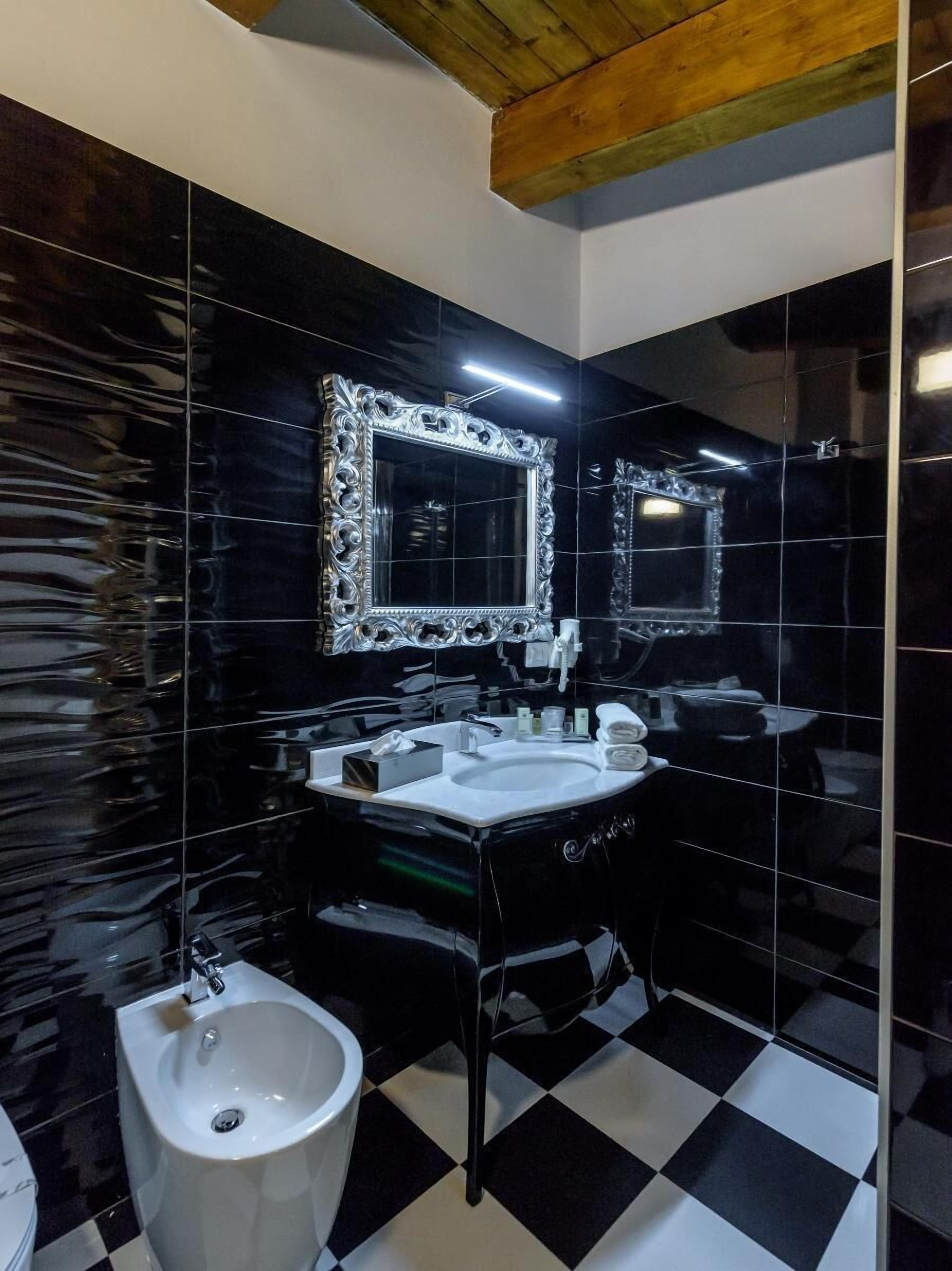 Une salle de bain moderne avec des carreaux de sol noirs et blancs formant un motif à damier, un lavabo blanc, un bidet et deux grands miroirs dotés de cadres décoratifs.