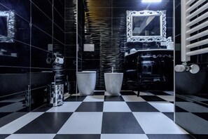 Une salle de bain moderne avec des carreaux de sol noirs et blancs formant un motif à damier, un grand miroir doté d’un cadre orné et une baignoire noire.