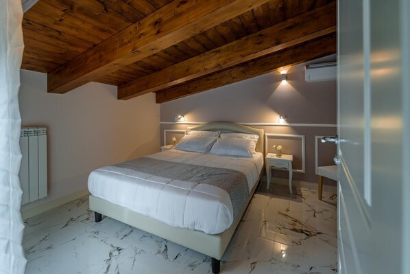 A bedroom with a bed, nightstands, a wall-mounted heater, and a marble floor.