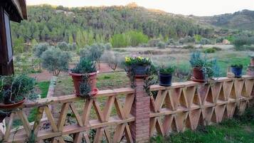 A wooden fence with potted plants, overlooking a hilly landscape with trees and shrubs.