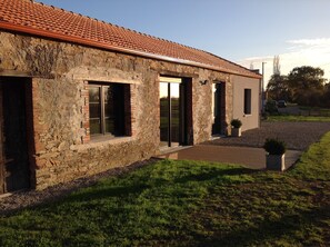 A stone building with a tiled roof, large windows, and a paved driveway. - Spacious, quiet vacation rental surrounded by nature, 15 minutes from the ocean and a half-hour from Nantes (Chéméré)