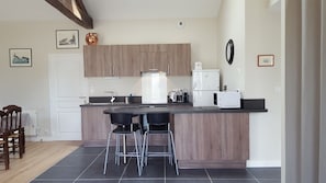 A modern kitchen with wooden cabinets, a black countertop, and a built-in stove. There are two bar stools and a white refrigerator. - Spacious, quiet vacation rental surrounded by nature, 15 minutes from the ocean and a half-hour from Nantes (Chéméré)