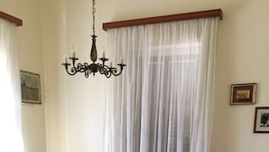 A living room with two black armchairs, a wooden coffee table, a chandelier, and a large window with sheer curtains.