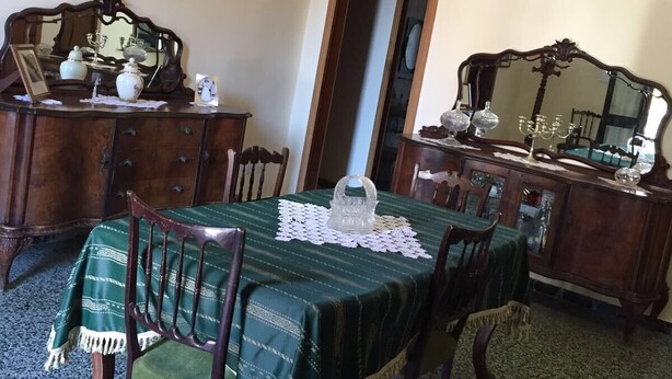 A dining room with a green tablecloth, wooden chairs, a chandelier, and a painting on the wall.