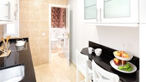 A modern kitchen with a black countertop, white cabinets, and a dining area with white chairs. There is a fruit bowl on the counter and a window above the cabinets. - CARRETAS APARTMENTS MADRID 102 (MADRID)