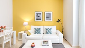 A modern living room with a yellow accent wall, white furniture, and two framed pictures. - CARRETAS APARTMENTS MADRID 102 (MADRID)