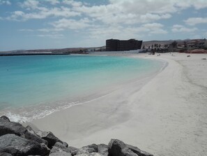 Une plage avec une eau turquoise et limpide, un rivage sablonneux et un promontoire rocheux au premier plan.