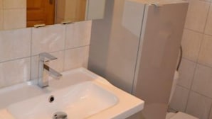 Ett badrum med ett vitt handfat, en spegel och en duschkabin.