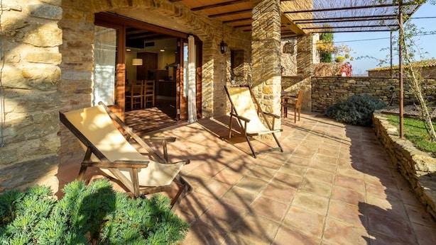 A stone patio with two wooden chairs and a table, a stone wall, and a pergola with vines. - RURAL HOUSE IN THE COSTA BRAVA (Sant Feliu De Boada)