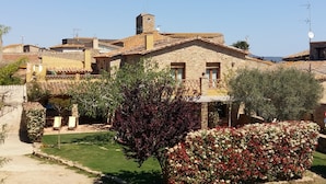 A stone building with a tiled roof, surrounded by greenery and a well-maintained lawn. - RURAL HOUSE IN THE COSTA BRAVA (Sant Feliu De Boada)