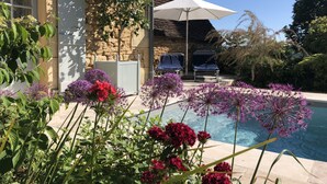 Zona junto a la piscina con un edificio de piedra, mobiliario exterior y plantas con flores.