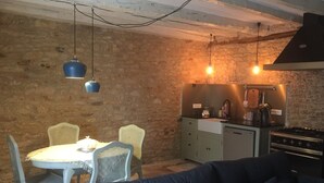 Una cocina acogedora con comedor, que cuenta con una pared de piedra, estufa y lámparas colgantes.