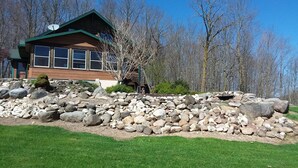 A cabin with a stone retaining wall and a grassy lawn. - Private home on twenty wooded acres. (Plymouth)