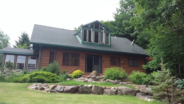 A log cabin with a gabled roof, a front porch, and a stone retaining wall. - Private home on twenty wooded acres. (Plymouth)