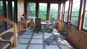 A wooden cabin with a dining area featuring a table and chairs, large windows, and a wooden staircase. - Private home on twenty wooded acres. (Plymouth)
