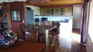 A dining area with wooden chairs and a table, a kitchen with wooden cabinets, and a staircase leading to an upper level. - Private home on twenty wooded acres. (Plymouth)