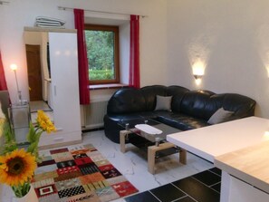 Una sala de estar con un sofá de cuero negro, una pequeña mesa de madera, un armario blanco y una alfombra acolchada.